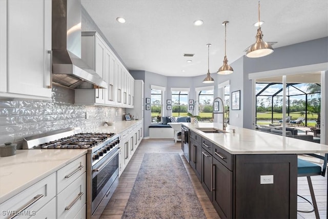 kitchen with stainless steel appliances, decorative backsplash, white cabinets, a sink, and wall chimney range hood