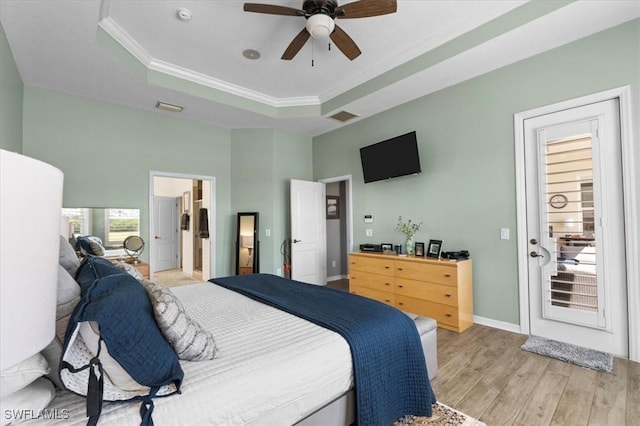 bedroom with a tray ceiling, visible vents, light wood-style floors, ornamental molding, and baseboards