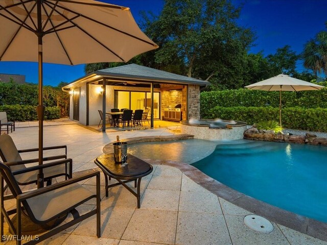 pool at twilight featuring an in ground hot tub and a patio area