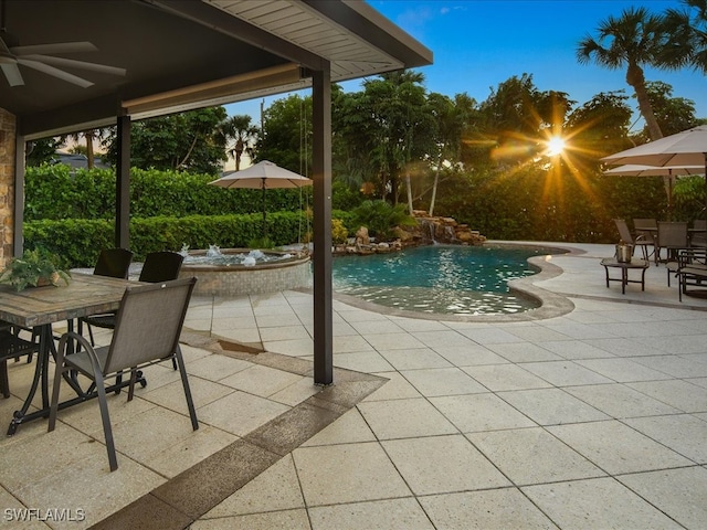 pool at dusk featuring ceiling fan and a patio area