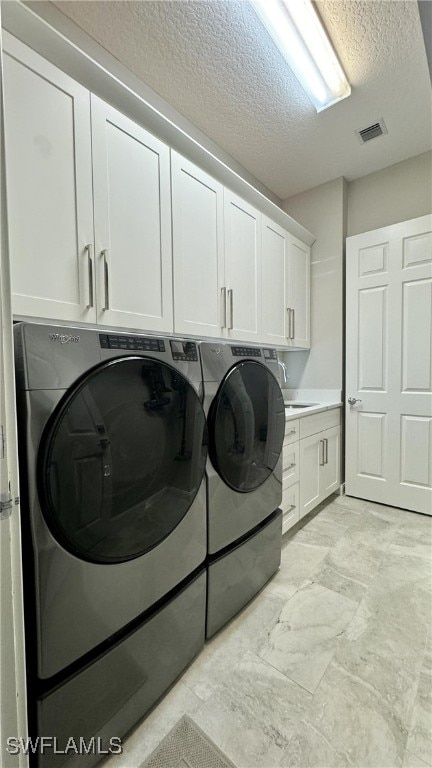 clothes washing area with cabinets, a textured ceiling, and washer and dryer