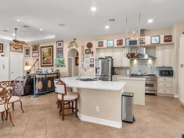 kitchen with stainless steel appliances, wall chimney range hood, a kitchen island with sink, and sink