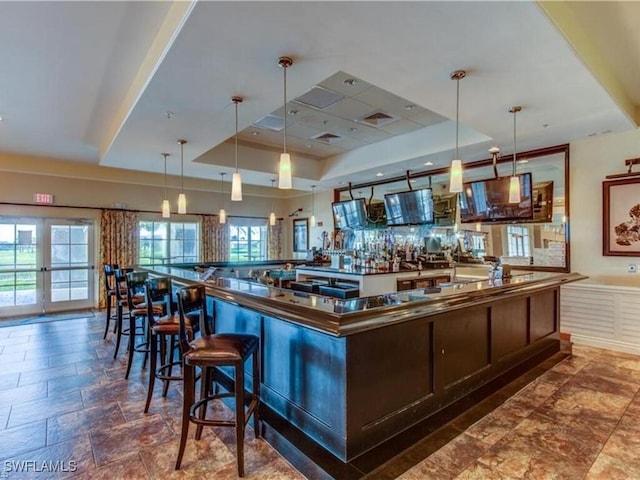 bar with dark brown cabinets, a raised ceiling, and hanging light fixtures