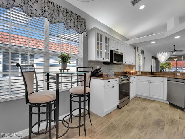 kitchen with kitchen peninsula, backsplash, appliances with stainless steel finishes, white cabinetry, and light hardwood / wood-style floors