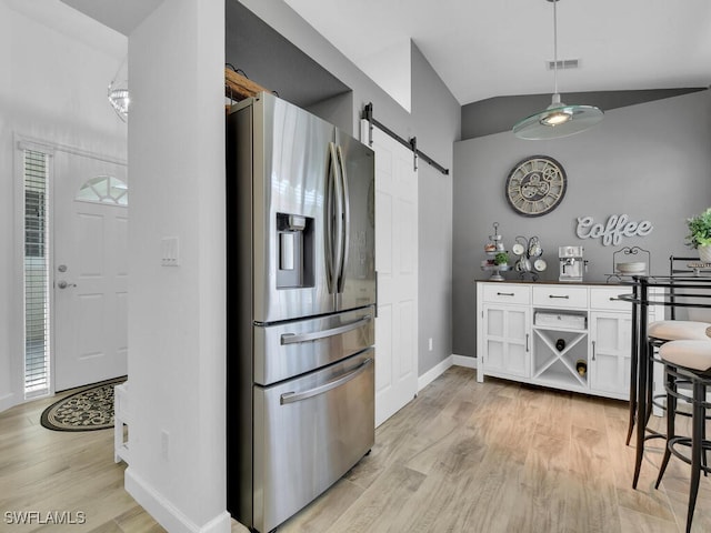 kitchen with lofted ceiling, light hardwood / wood-style flooring, stainless steel fridge, a barn door, and white cabinets