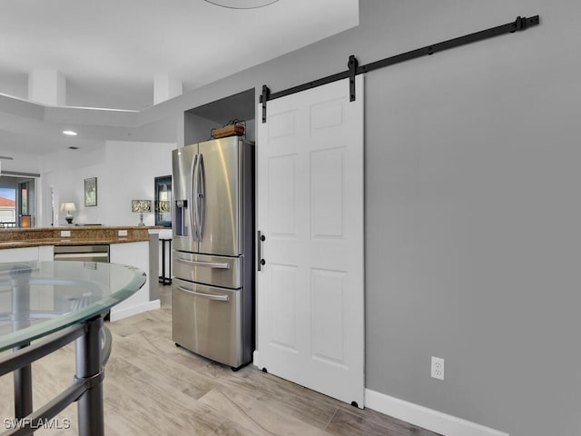 kitchen with light hardwood / wood-style floors, a barn door, and stainless steel refrigerator with ice dispenser