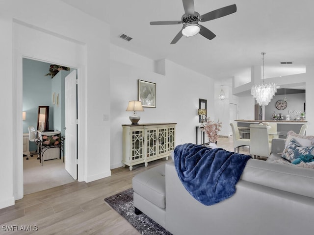 living room with lofted ceiling, light hardwood / wood-style flooring, and ceiling fan with notable chandelier