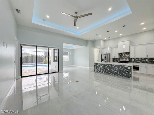 kitchen featuring appliances with stainless steel finishes, decorative backsplash, white cabinets, a tray ceiling, and ceiling fan