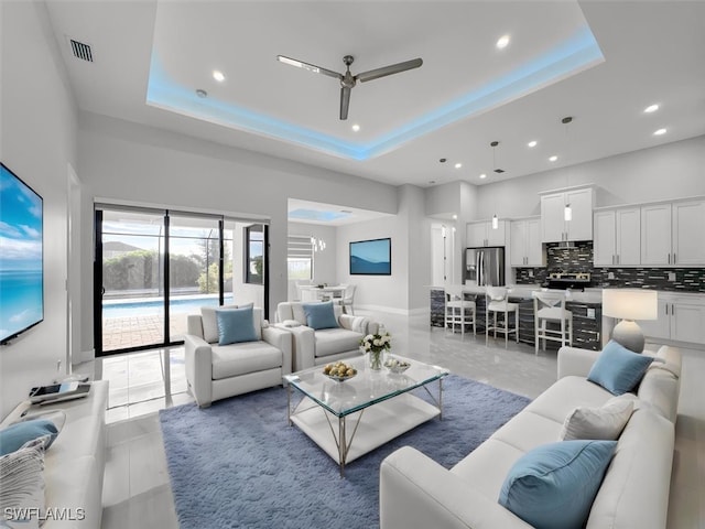 living room featuring ceiling fan, a raised ceiling, and light tile patterned floors