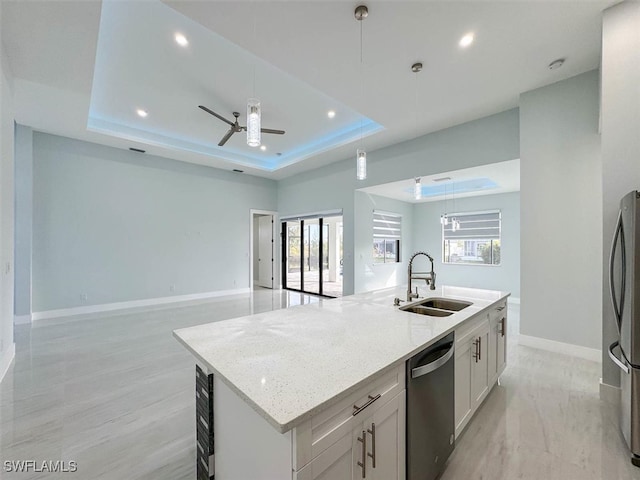 kitchen with appliances with stainless steel finishes, white cabinetry, light stone counters, a kitchen island with sink, and sink