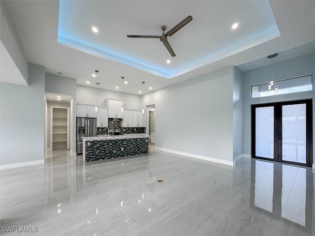 unfurnished living room with a tray ceiling, ceiling fan, and french doors