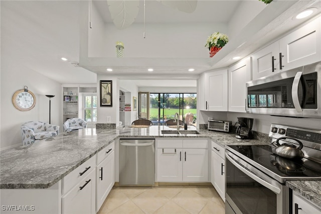 kitchen with white cabinets, kitchen peninsula, light stone countertops, stainless steel appliances, and sink