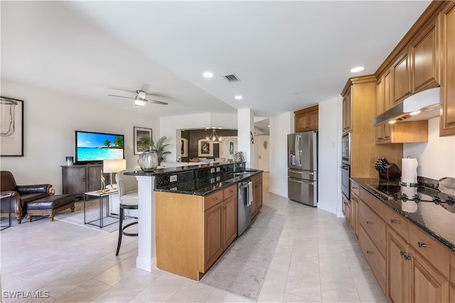 kitchen with sink, stainless steel appliances, dark stone countertops, ceiling fan with notable chandelier, and a kitchen bar