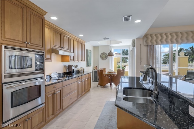 kitchen featuring light tile patterned flooring, dark stone counters, decorative light fixtures, sink, and stainless steel appliances