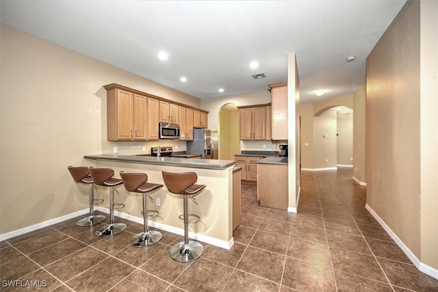 kitchen with appliances with stainless steel finishes, kitchen peninsula, a kitchen breakfast bar, and dark tile patterned flooring