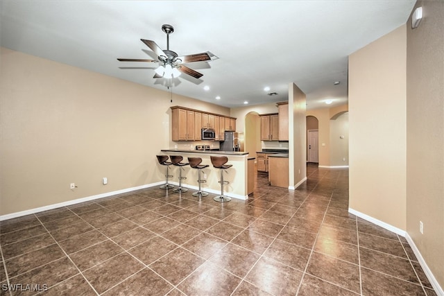 kitchen with ceiling fan, kitchen peninsula, dark tile patterned floors, stainless steel appliances, and a breakfast bar