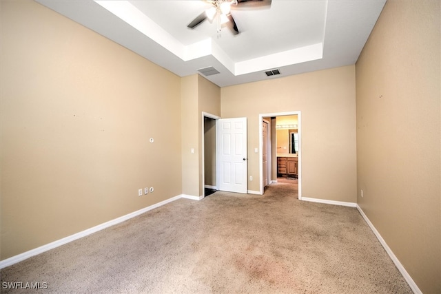 unfurnished bedroom featuring ceiling fan, a raised ceiling, and light carpet