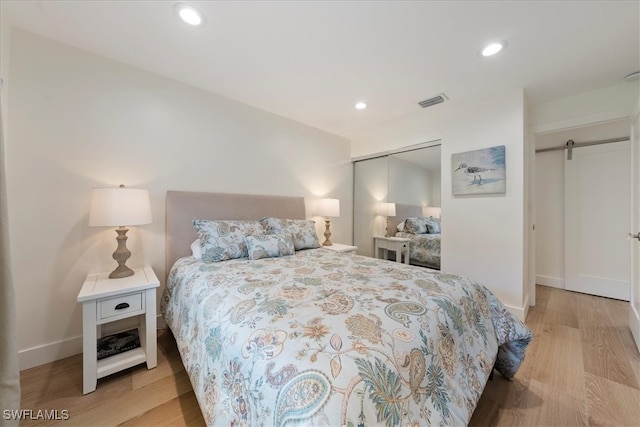 bedroom with a barn door, light hardwood / wood-style floors, and a closet