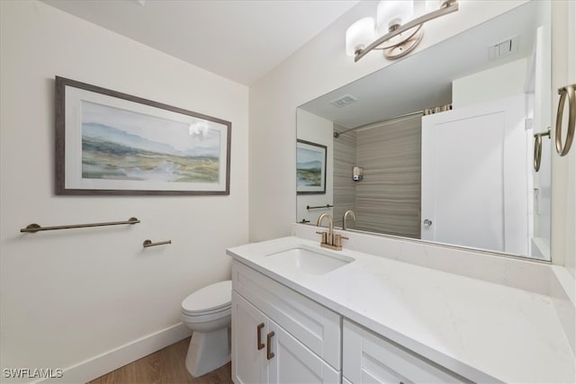 bathroom with wood-type flooring, vanity, a tile shower, and toilet