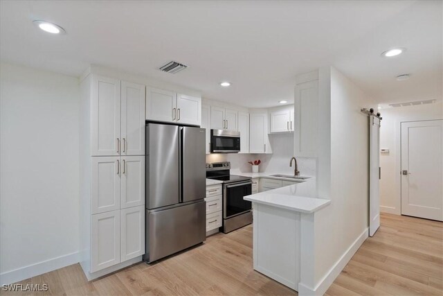 kitchen featuring white cabinetry, sink, stainless steel appliances, a barn door, and light wood-type flooring