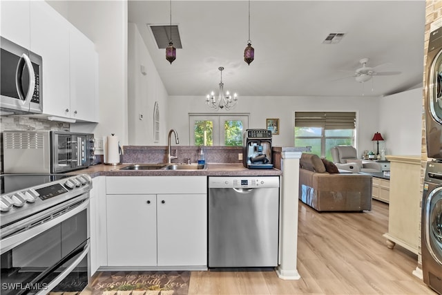 kitchen with white cabinets, stacked washing maching and dryer, appliances with stainless steel finishes, and light hardwood / wood-style flooring