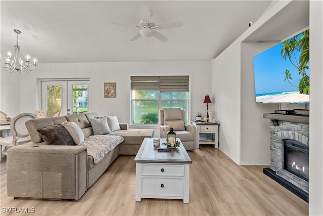 living room featuring ceiling fan with notable chandelier, light hardwood / wood-style floors, a stone fireplace, and a wealth of natural light