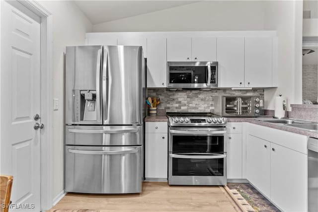 kitchen with white cabinetry, light hardwood / wood-style flooring, appliances with stainless steel finishes, and vaulted ceiling