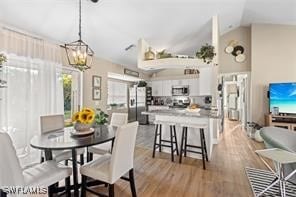 dining room with a notable chandelier, light wood-type flooring, and vaulted ceiling