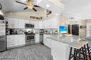 kitchen with appliances with stainless steel finishes, white cabinetry, a kitchen breakfast bar, and vaulted ceiling