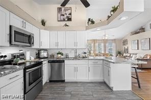 kitchen with appliances with stainless steel finishes, kitchen peninsula, white cabinetry, and a kitchen breakfast bar