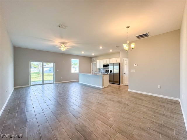 unfurnished living room with ceiling fan with notable chandelier and light hardwood / wood-style floors