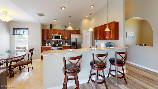 kitchen with appliances with stainless steel finishes, a kitchen breakfast bar, kitchen peninsula, light wood-type flooring, and decorative light fixtures