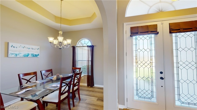 dining room featuring wood-type flooring, a chandelier, french doors, and a raised ceiling