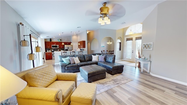 living room with ceiling fan, vaulted ceiling, light wood-type flooring, and french doors