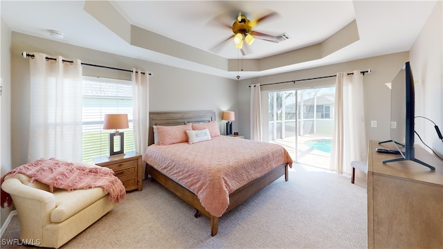 carpeted bedroom with a tray ceiling, ceiling fan, and access to exterior