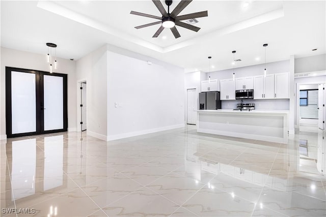 unfurnished living room with ceiling fan, a raised ceiling, and french doors