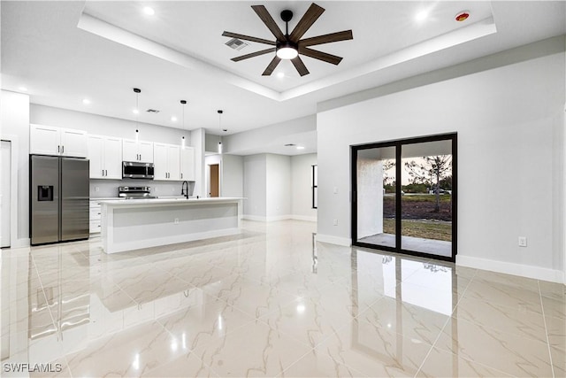 kitchen featuring hanging light fixtures, stainless steel appliances, a raised ceiling, a kitchen island with sink, and white cabinets