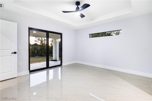 empty room with ceiling fan, a wealth of natural light, and a tray ceiling