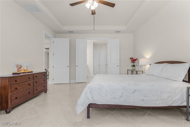 tiled bedroom with ceiling fan and a tray ceiling