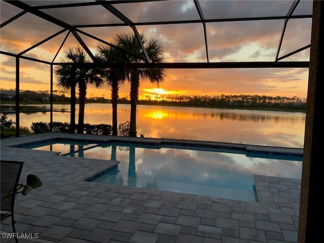 pool at dusk with a patio, a water view, and a lanai