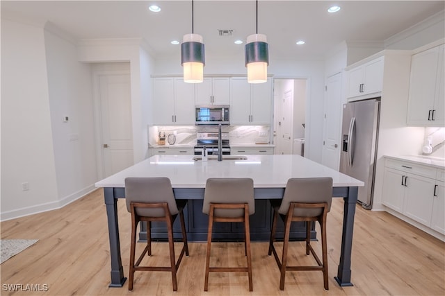 kitchen featuring hanging light fixtures, light hardwood / wood-style floors, an island with sink, stainless steel appliances, and sink