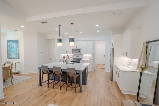 kitchen featuring a kitchen island with sink, white cabinetry, light hardwood / wood-style flooring, appliances with stainless steel finishes, and decorative light fixtures