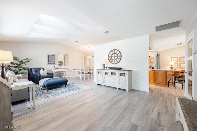 living room featuring light hardwood / wood-style flooring, lofted ceiling, and a notable chandelier