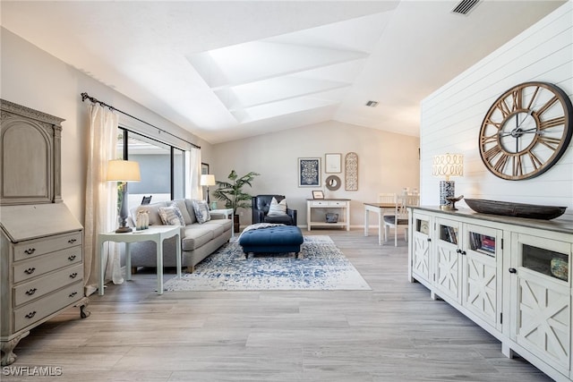 living room featuring wood walls, vaulted ceiling with skylight, and light hardwood / wood-style floors