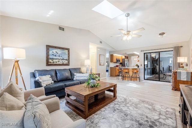 living room with vaulted ceiling with skylight, ceiling fan, and light hardwood / wood-style flooring