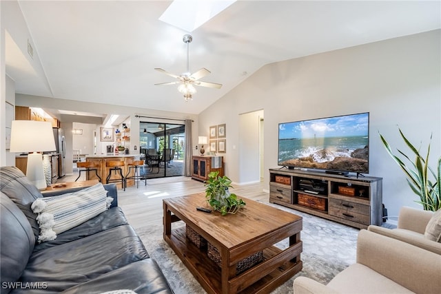 living room with vaulted ceiling with skylight, ceiling fan, and light hardwood / wood-style floors