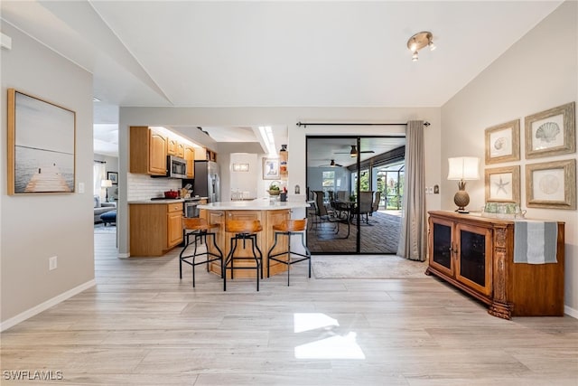 kitchen with light hardwood / wood-style floors, kitchen peninsula, a kitchen breakfast bar, backsplash, and appliances with stainless steel finishes