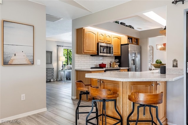 kitchen featuring stainless steel appliances, a kitchen bar, decorative backsplash, kitchen peninsula, and light hardwood / wood-style flooring