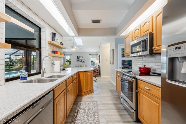 kitchen featuring sink, appliances with stainless steel finishes, backsplash, a skylight, and light hardwood / wood-style flooring