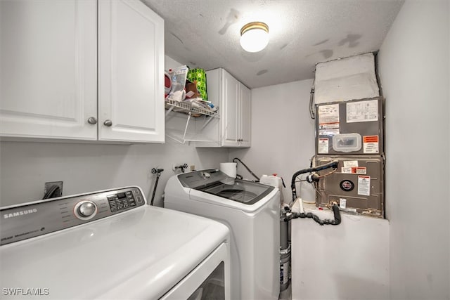 laundry area with a textured ceiling, separate washer and dryer, heating unit, and cabinets